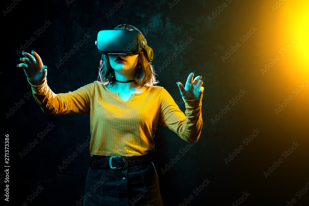 Young hipster woman with curly hair wearing virtual reality goggles and touch another world in studio neon lights. Smartphone using with VR headset.