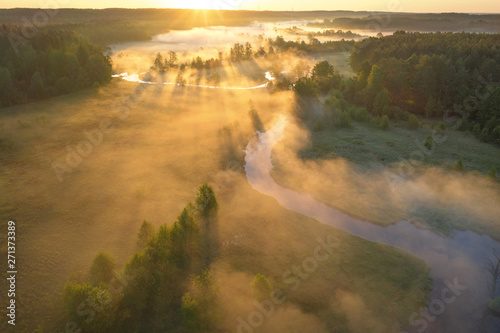 Sunrise over foggy river. Aerial view of river nature in sunlight. Bright sunny morning landscape view from above. Sunrays through mist on meadow