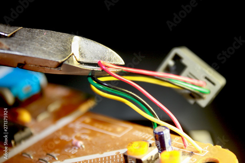 Electrical board with electronic components. High-tech printed circuit board. Cutting the electric wire with wire cutters
