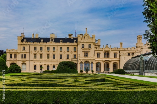 Lednice, Czech Republic - May 28 2019: Famous Lednice castle in South Moravia with yellow facade. Garden with green lawn, bushes, trees and greenhouse. Sunny spring day, blue sky, white clouds.