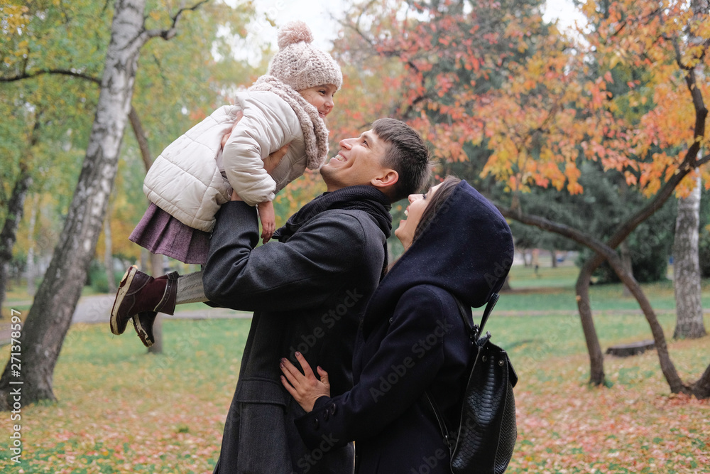 Family on a walk in the park during the first snow. Happy father and mother playing with daughter, throws the girl up in the sky. The emotion of happiness, fun, love.