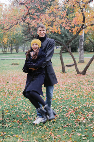 Smiling lovers hold hands and look at each other. A man and a woman in a black coat on background of autumn park.