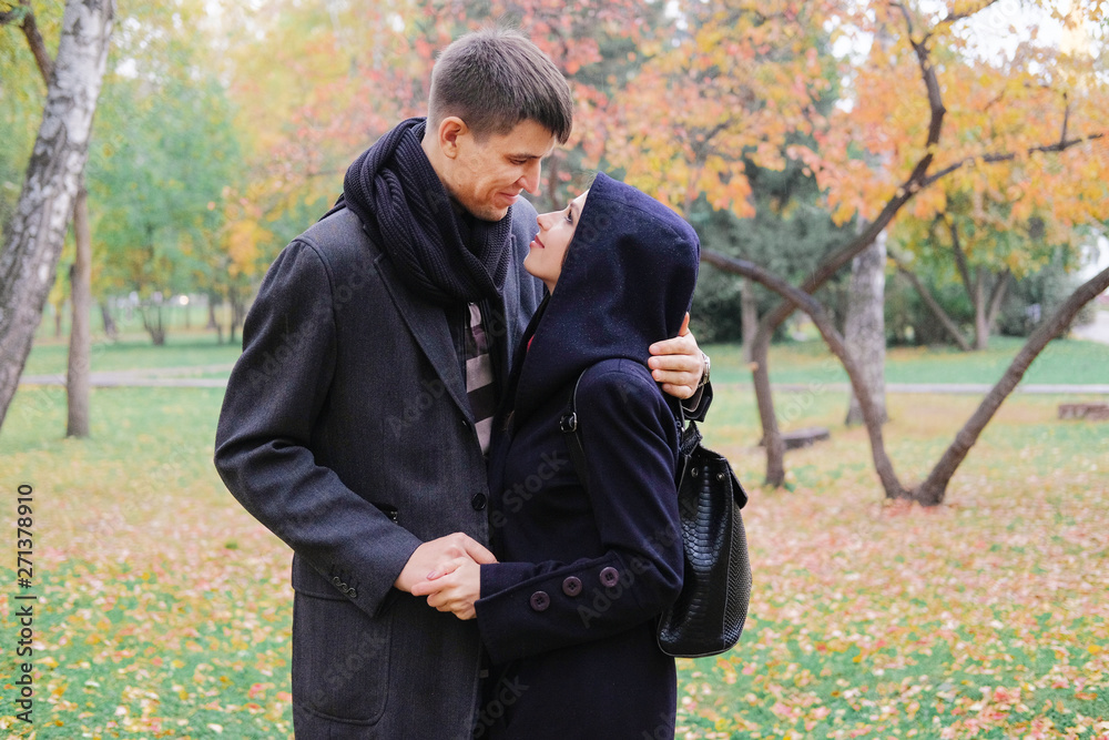 Smiling lovers hold hands and look at each other. A man and a woman in a black coat on background of autumn park. Smiling lovers hold hands and look at each other. A man and a woman in a black coat on background of autumn park.