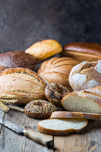Assortment of fresh baked bread and buns on wooden table background