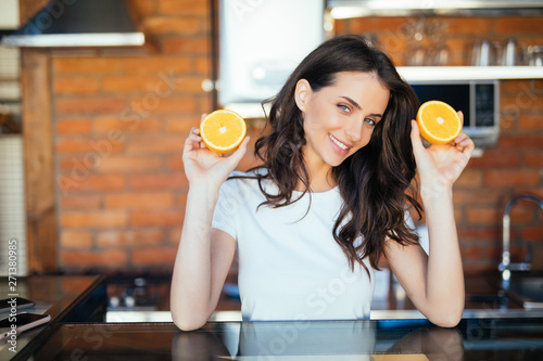 Beautiful young woman holding sliced orange fruit and cooking food in the kitchen