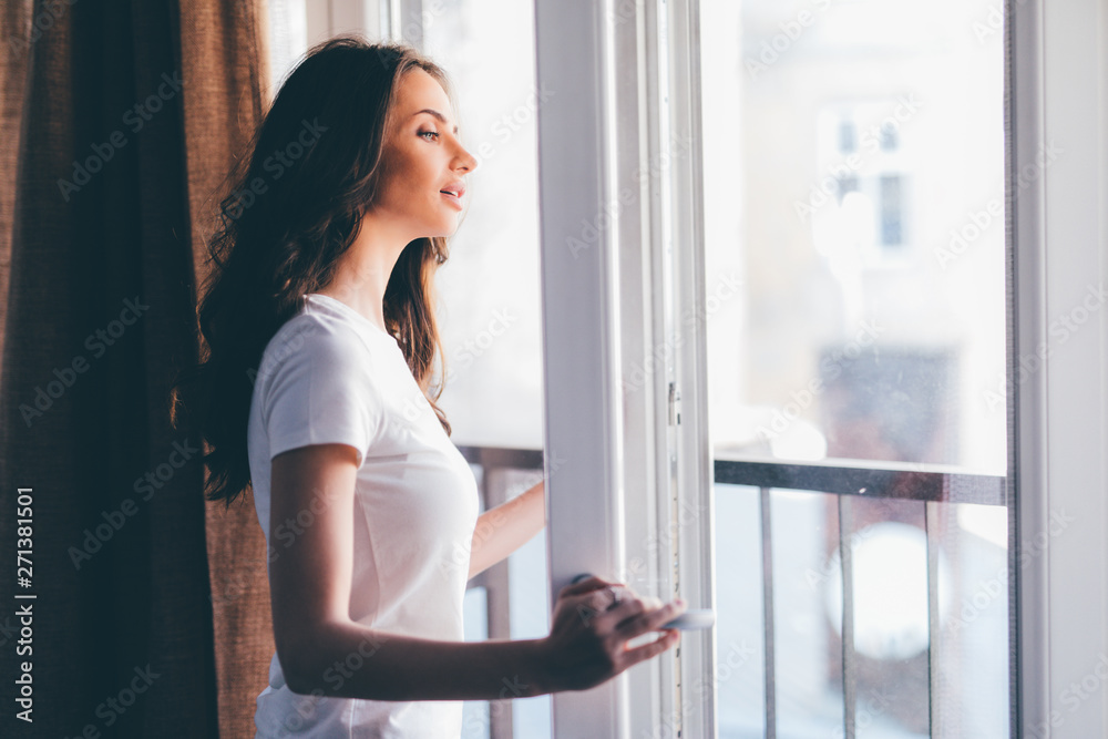 Young woman in a white shirt stands in the open doorway balcony Young woman in a white shirt stands in the open doorway balcony