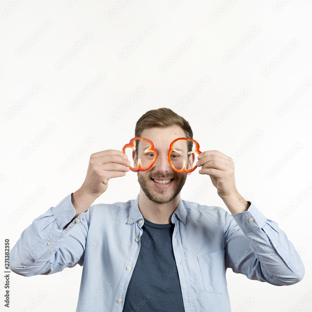 Portrait of happy man holding bell peppers slices in front of his eyes Portrait of happy man holding bell peppers slices in front of his eyes