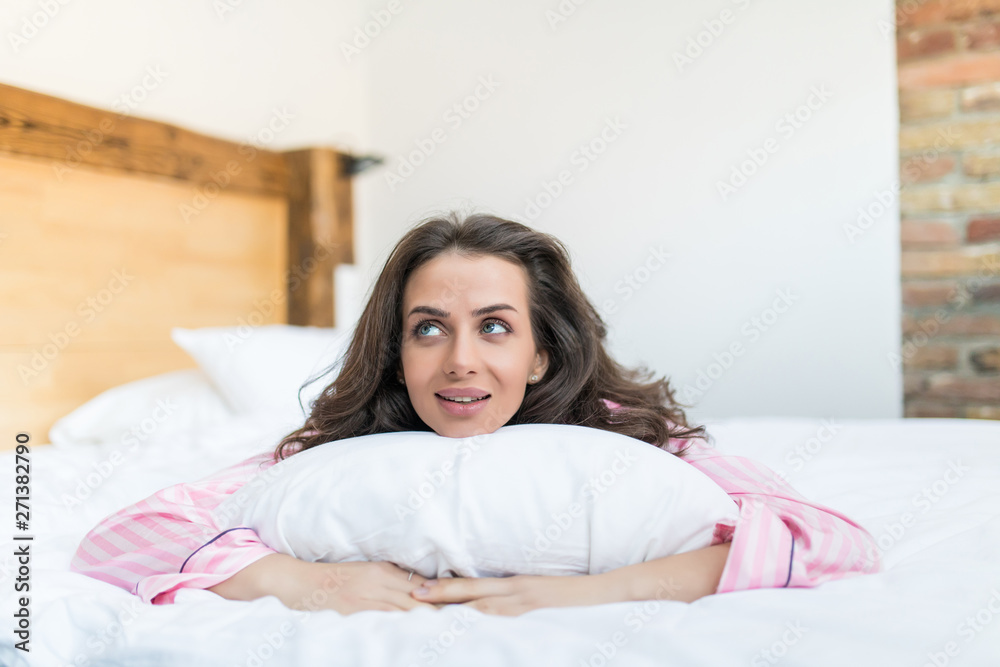 Beautiful young woman lying with comfortable pillow on bed at home Beautiful young woman lying with comfortable pillow on bed at home