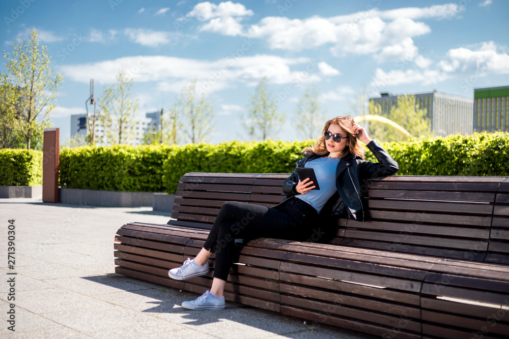 Woman sitting on bench among urban space and using tablet in the city Woman sitting on bench among urban space and using tablet in the city