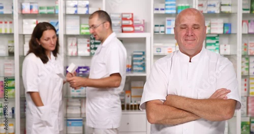 One Pharmacist Smiling to Camera and Two Pharmacists Talking in Background