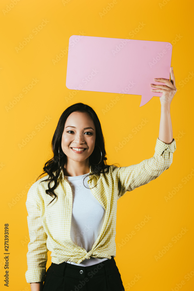 attractive asian woman holding pink speech bubble, isolated on yellow attractive asian woman holding pink speech bubble, isolated on yellow