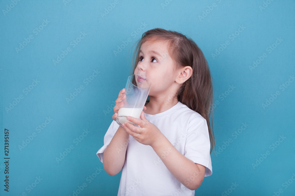 Cute little girl drinking milk from glass on blue background Cute little girl drinking milk from glass on blue background