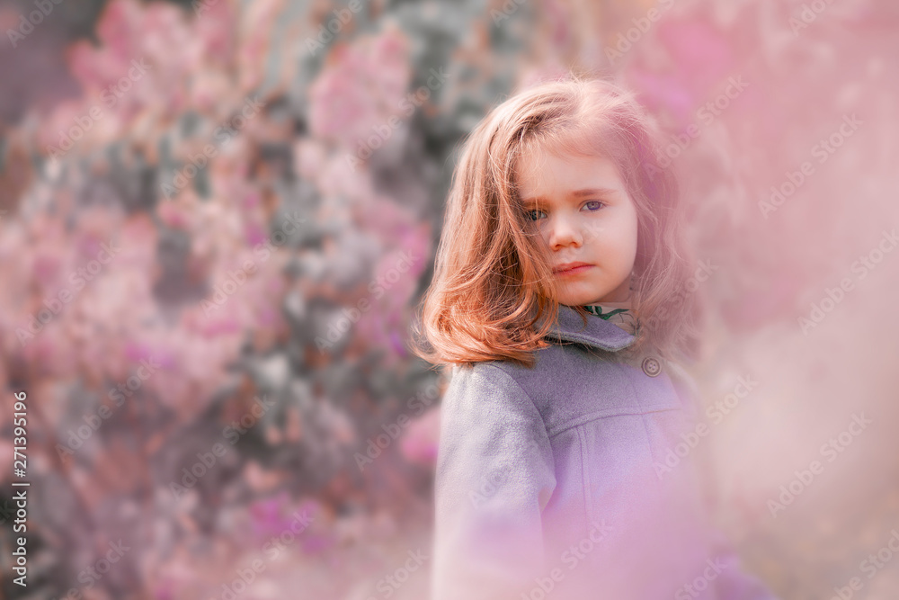 Little red-haired girl stands in lilac bushes