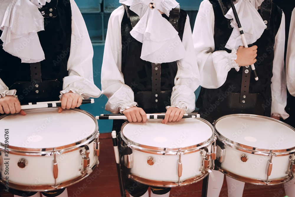Obraz premium A closeup of the hands of a drummer at a parade. Children's ensemble in white shirts. White new snare drum, white sticks. The concept of a military parade and march.