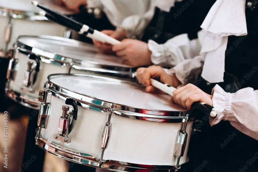 Obraz premium A closeup of the hands of a drummer at a parade. Children's ensemble in white shirts. White new snare drum, white sticks. The concept of a military parade and march.