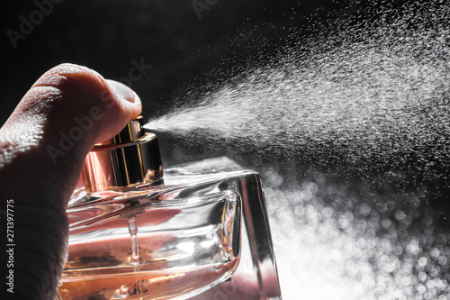 spraying perfume on dark background, closeup photo