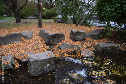 Rocks and trees next to pond in park with yellow brown leaves autumn winter colours
