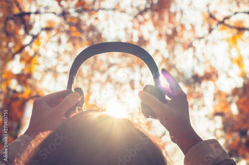 Female with headphones walking on the park listen sounds or music of autumn forest. Concept. Indian summer season
