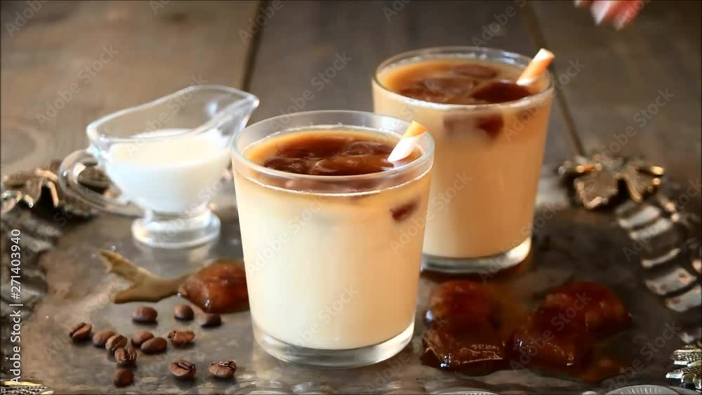Iced cold latte coffee with ice cubes and coffee beans. Woman's hand puts in a glass cocktail paper straws. Iced cold latte coffee with ice cubes and coffee beans. Woman's hand puts in a glass cocktail paper straws.