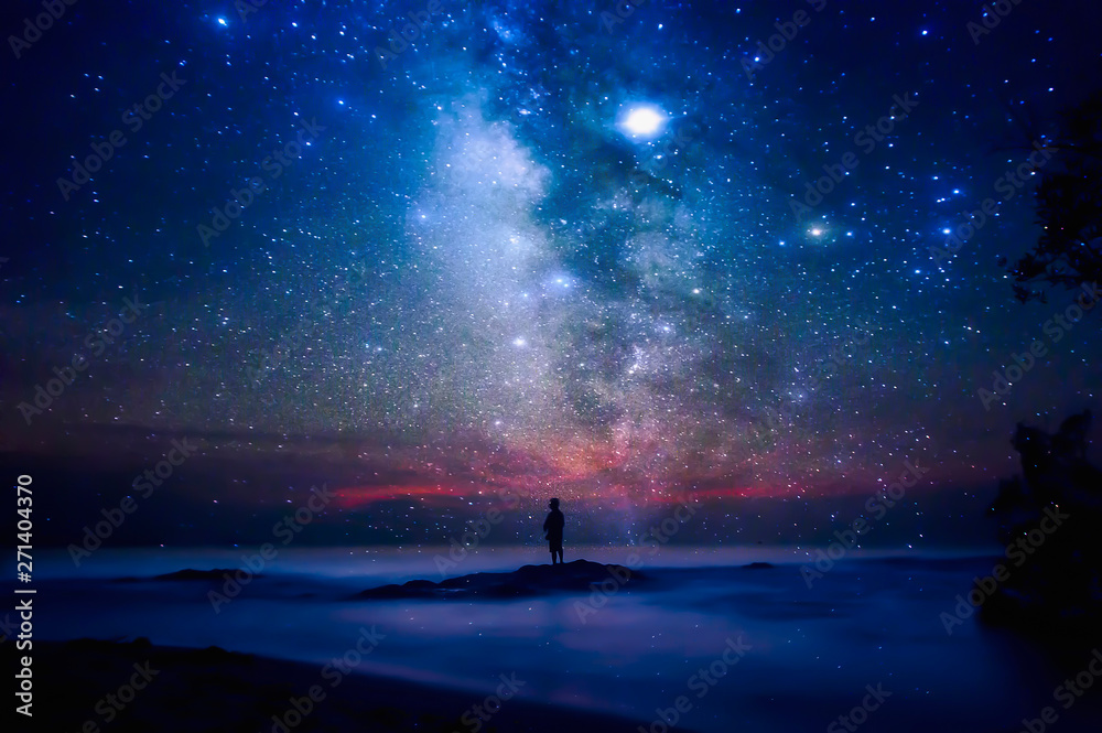 Starry night sky over sea and beach with man silhouette. man standing on sea beach under starry sky. - obrazy, fototapety, plakaty 