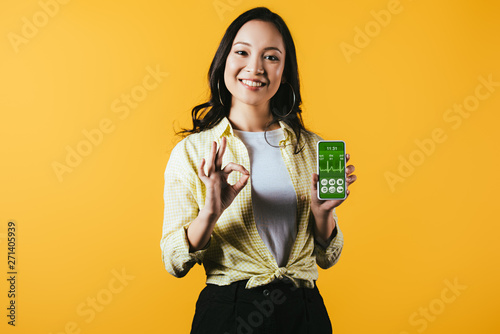smiling asian girl showing ok sign and smartphone with health app, isolated on yellow