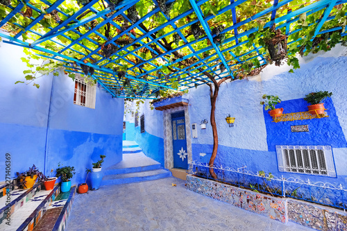 Typical beautiful moroccan architecture in Chefchaouen blue city medina in Morocco with blue walls, details, colorful flower pots and household items © Andrii Vergeles