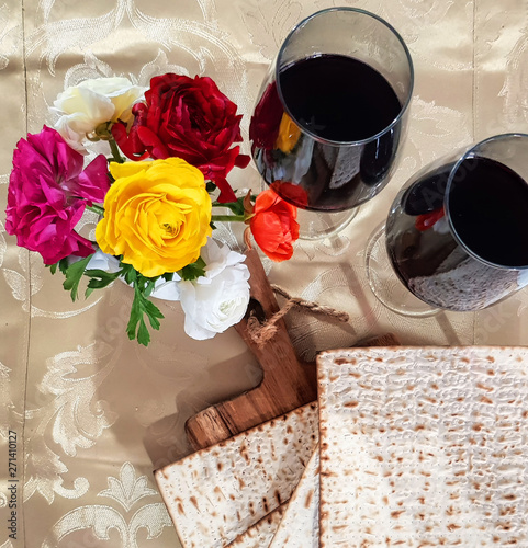 Pesach Holiday. Traditional matzo or matzoh, red wine in the glass and beautiful spring flowers on the table covered with a festive tablecloth photo