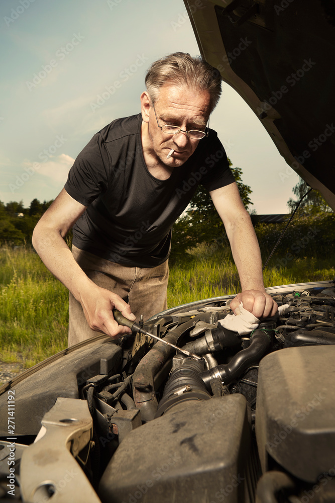 Aging man trying to fix broken car engine on lonely way