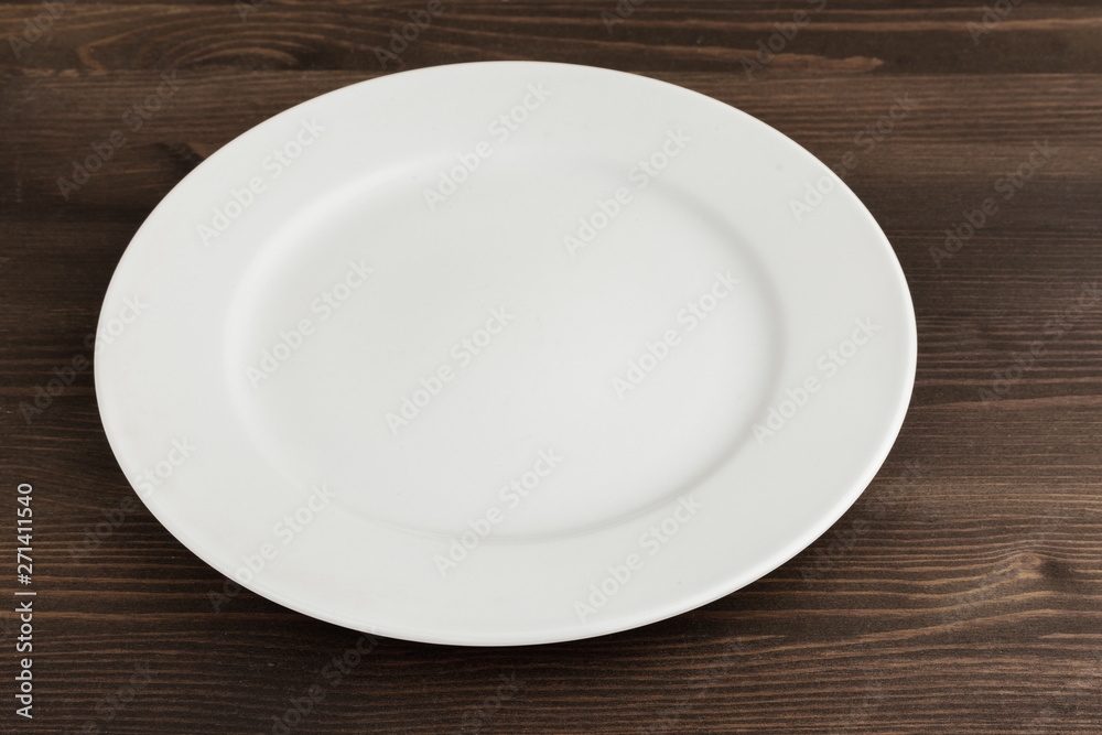White round china plate on a wooden brown table. White round china plate on a wooden brown table.
