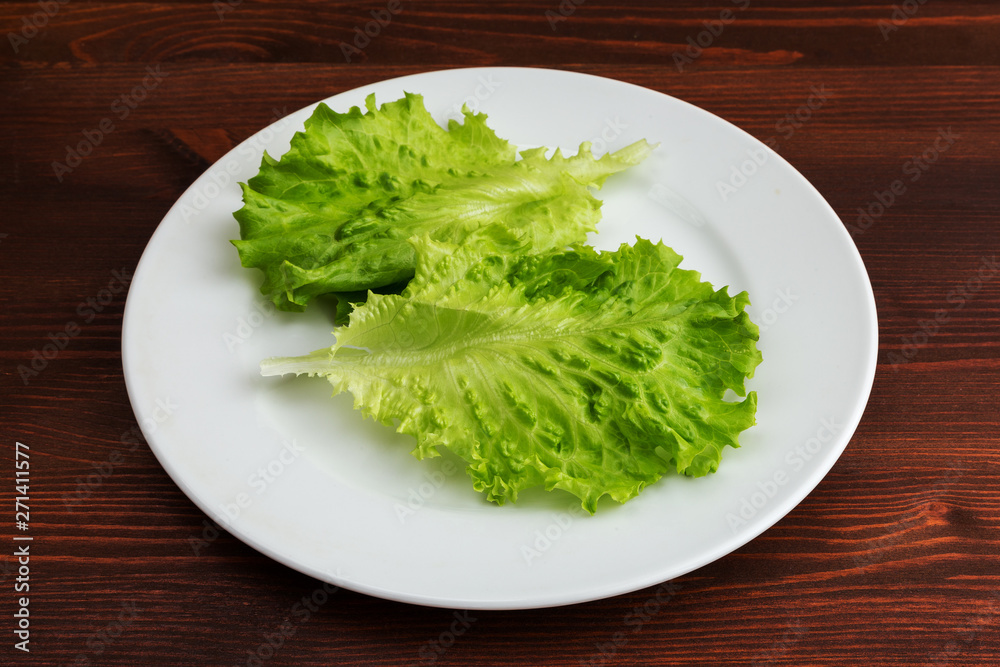 Slices of boiled potatoes, two tomatoes and a leaf of parsley, lie on a white round plate on a wooden brown table.