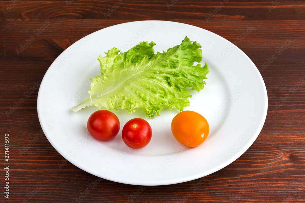 Green leaf lettuce and tomatoes on a white plate on a wooden table. Green leaf lettuce and tomatoes on a white plate on a wooden table.