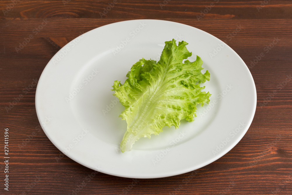 Green leaf of lettuce on a white plate on a wooden table. Green leaf of lettuce on a white plate on a wooden table.