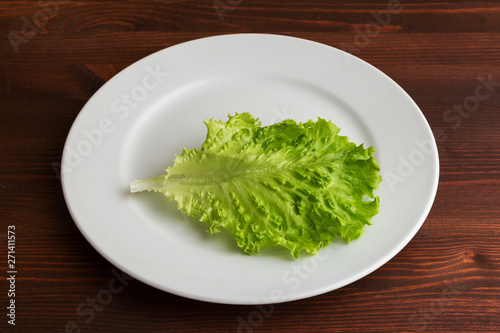 Slices of boiled potatoes  two tomatoes and a leaf of parsley  lie on a white round plate on a wooden brown table.