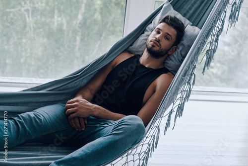 Time to relax. Handsome young man in casual clothing looking at camera while lying in the hammock indoors