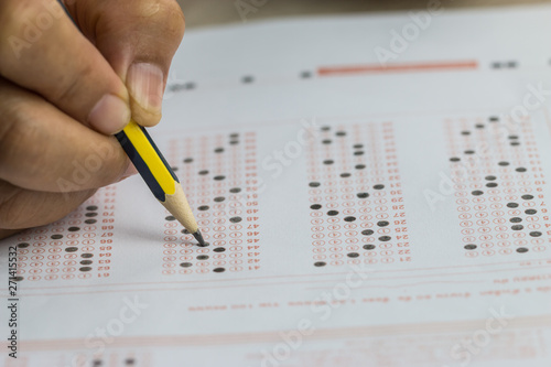 School or university students hands taking exams, writing examination room with holding pencil on optical form answers paper sheet on desk doing final test in classroom. Education assessment Concept photo