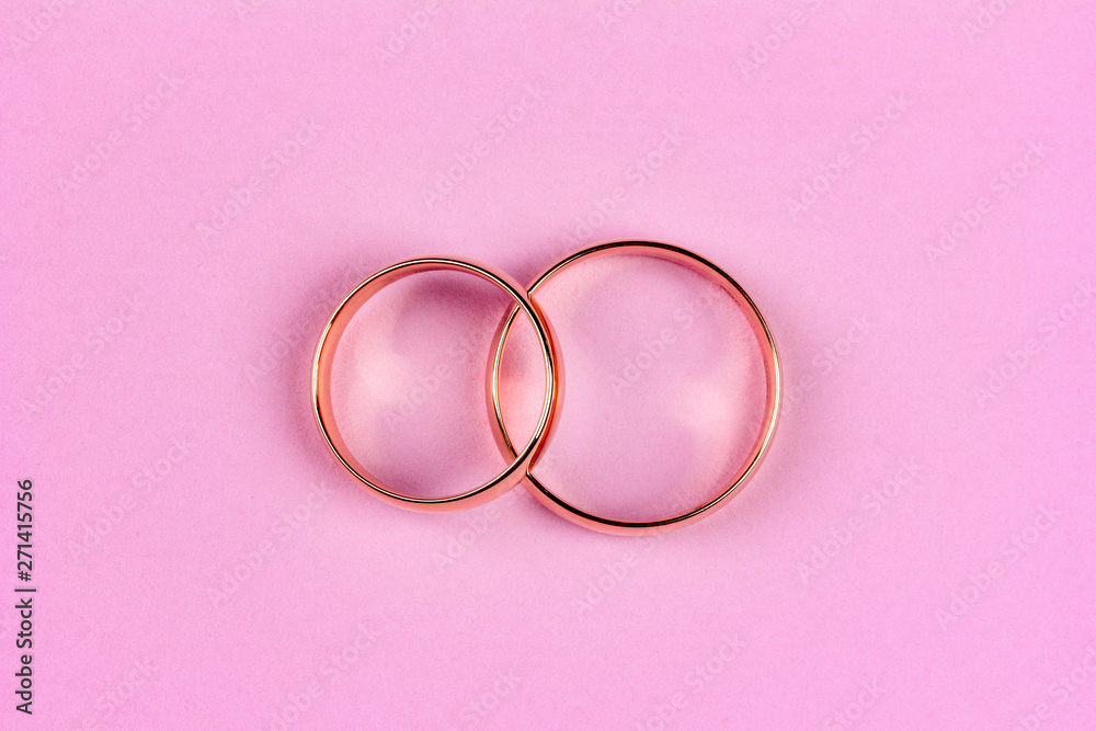 a pair of gold wedding rings on a pink background, top view flat lay a pair of gold wedding rings on a pink background, top view flat lay