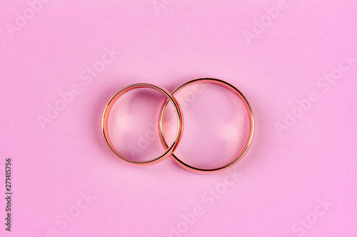a pair of gold wedding rings on a pink background, top view flat lay