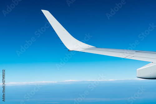 Wing of plane over white clouds. Airplane flying on blue sky. Scenic view from airplane window. Commercial airline flight. Plane wing above clouds. Flight mechanics concept. International flight.