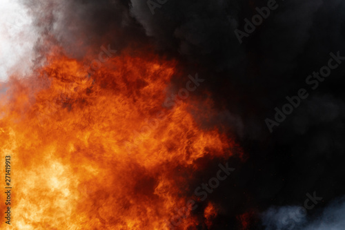 Dangerous flames of red-orange fire, motion clouds of black smoke covered sky. Defocus, motion blur, haze from strong fire and high temperature from flames. Atmospheric and smoke dispersion.