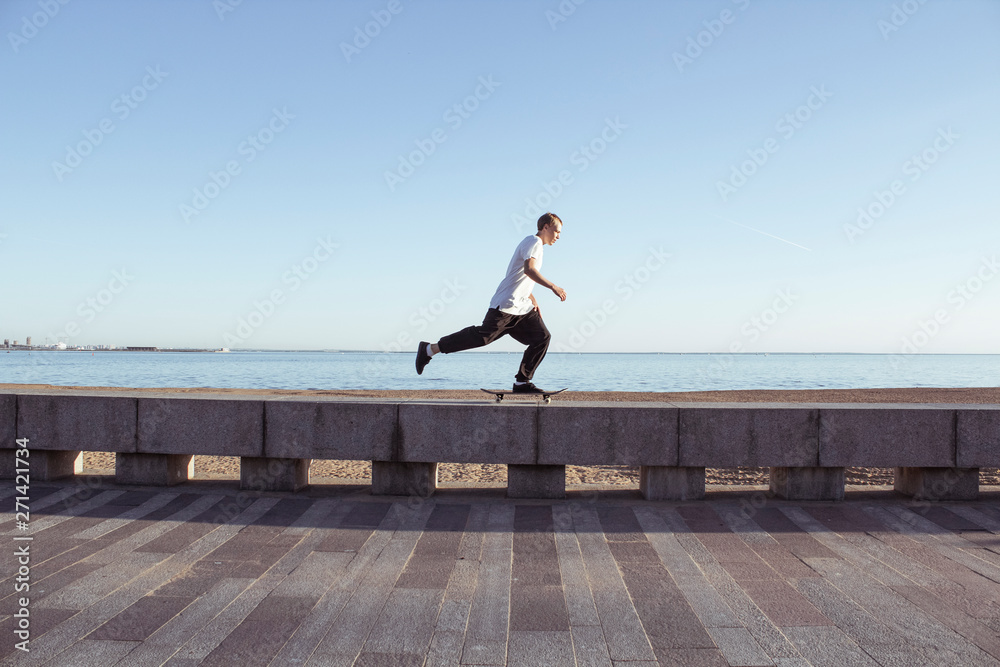 Skater rides on the parapet against the backdrop of the sea and the beach. Young european guy on a skateboard. Summer extreme sport skateboarding. Street style. Skater rides on the parapet against the backdrop of the sea and the beach. Young european guy on a skateboard. Summer extreme sport skateboarding. Street style.