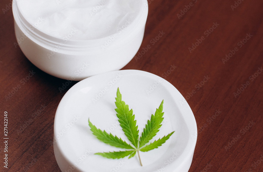 Moisturizing hemp hand cream in dose with green cannabis leaf. Cannabis cosmetics. Cream from biological and ecological plants of hemp vegetable pharmaceutical oil CBD Moisturizing hemp hand cream in dose with green cannabis leaf. Cannabis cosmetics. Cream from biological and ecological plants of hemp vegetable pharmaceutical oil CBD