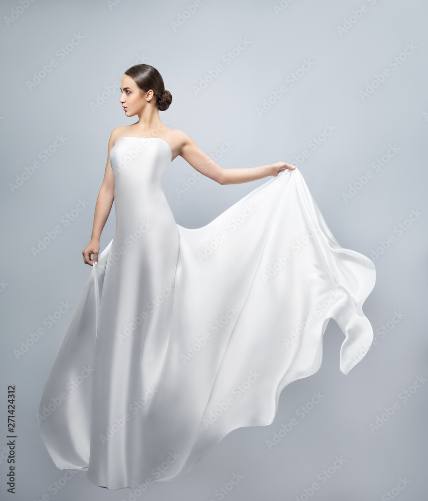 Fashion portrait of a beautiful woman in a waving white dress. Light fabric flies in the wind. Fashion portrait of a beautiful woman in a waving white dress. Light fabric flies in the wind.