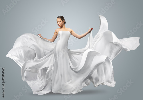 Fashion portrait of a beautiful woman in a waving white dress. Light fabric flies in the wind.