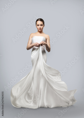beautiful woman in a light fluttering white dress. Light fabric flies in the wind. Light gray background.