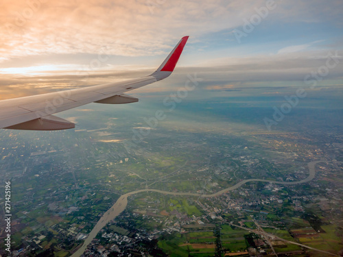 View from airplane window to see sky on  Morning sunrise with Wing of an airplane.In Thailand, below is the Chao Phraya River and the rice fields and houses of the people.