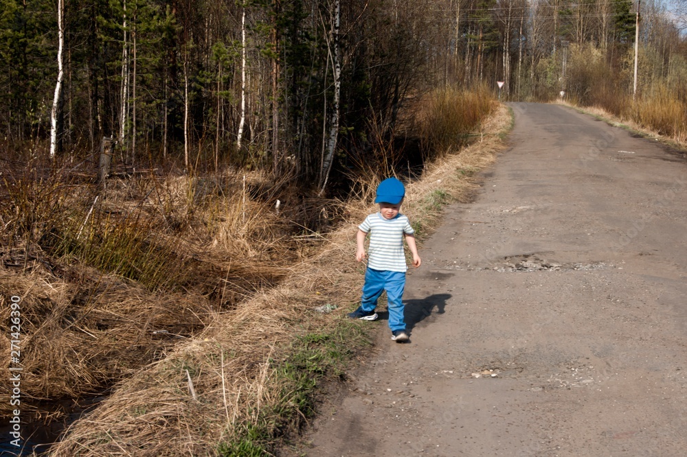 Fototapeta premium Early spring, a little boy of three years old in blue pants, one on a country road
