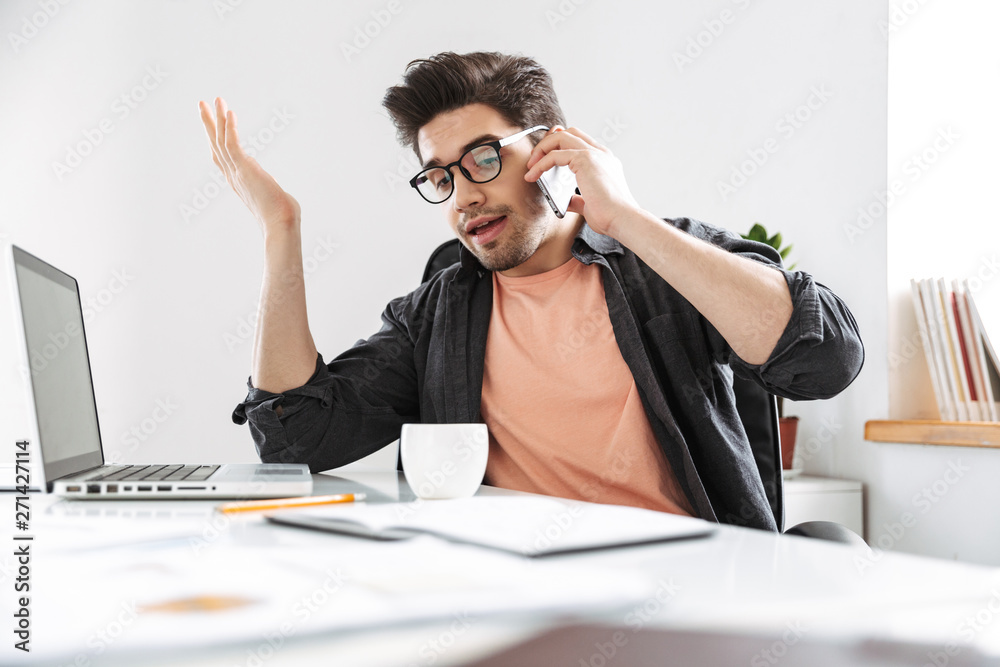 Displeased handsome man in eyeglasses talking by smartphone Displeased handsome man in eyeglasses talking by smartphone