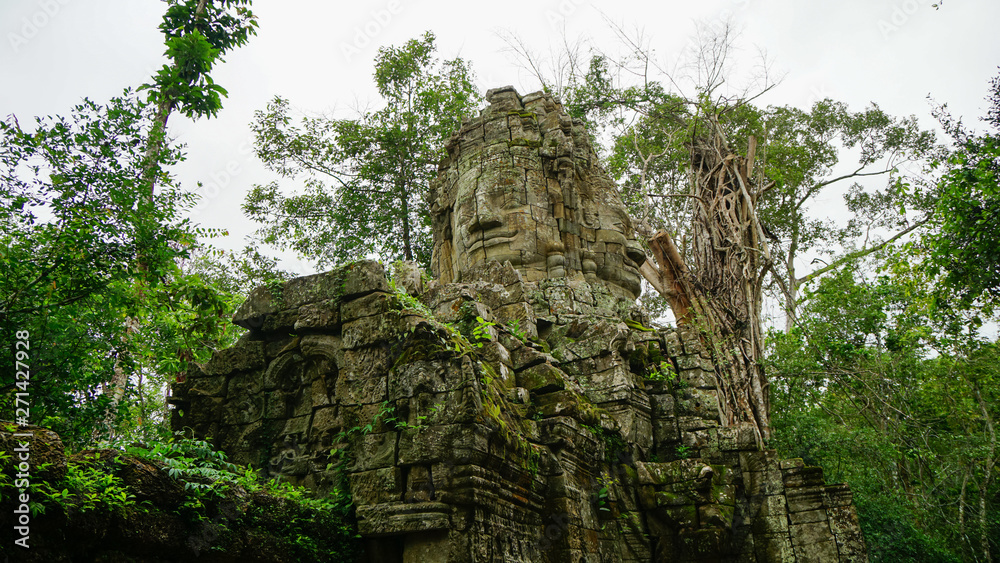 Historic Buddha head and face shot from low angle on with the jungle around the ancient statue at one of the ruined temples at Angkor Thom (Angkor Wat, UNESCO World Heritage Site, Siem Reap, Cambodia)