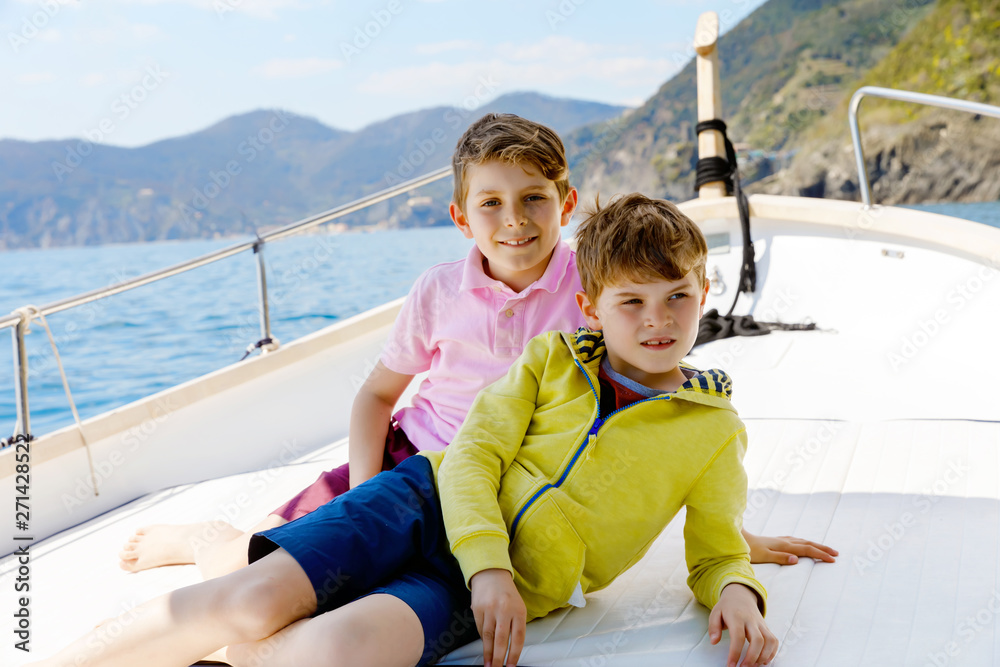 Two little kid boys, best friends enjoying sailing boat trip. Family vacations on ocean or sea on sunny day. Children smiling. Brothers, schoolchilden, siblings, best friends having fun on yacht.