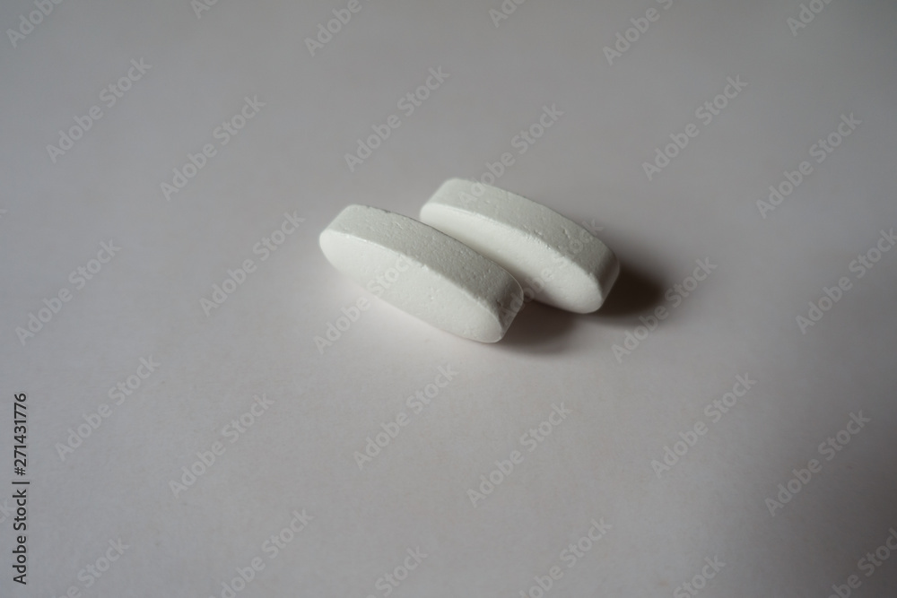 Close view of 2 big white oblong caplets of calcium citrate Close view of 2 big white oblong caplets of calcium citrate